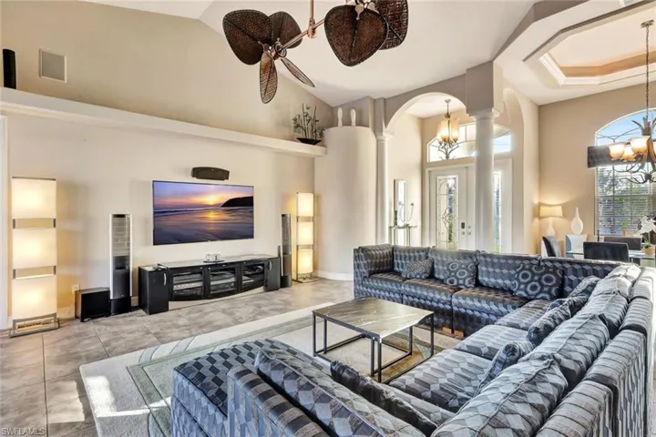 Tiled living room featuring ceiling fan with notable chandelier, a towering ceiling, and decorative columns