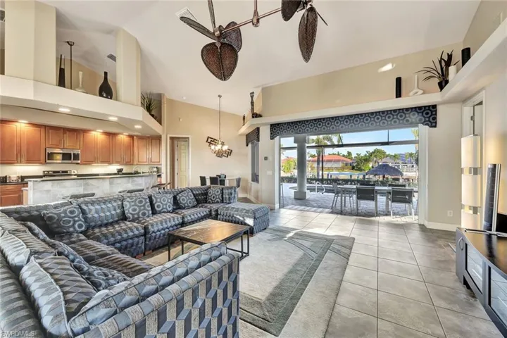 Tiled living room with ceiling fan with notable chandelier and a high ceiling