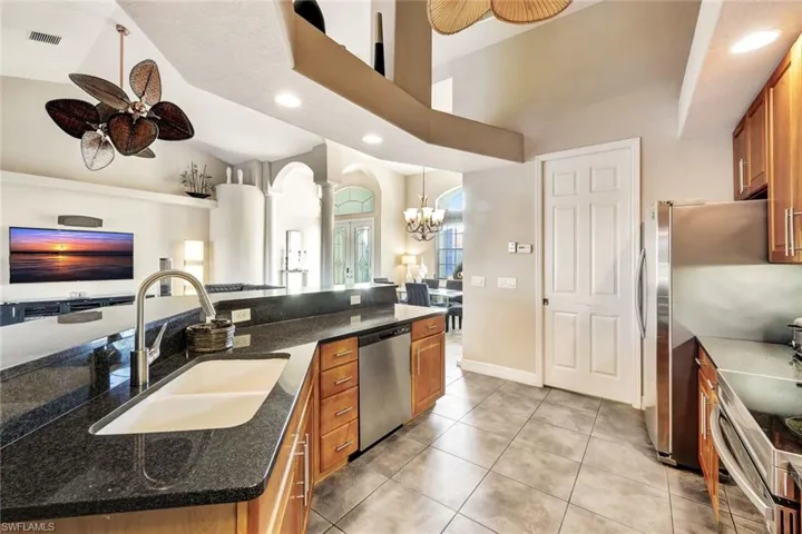 Kitchen featuring dark stone counters, a large island with sink, ceiling fan with notable chandelier, sink, and stainless steel appliances