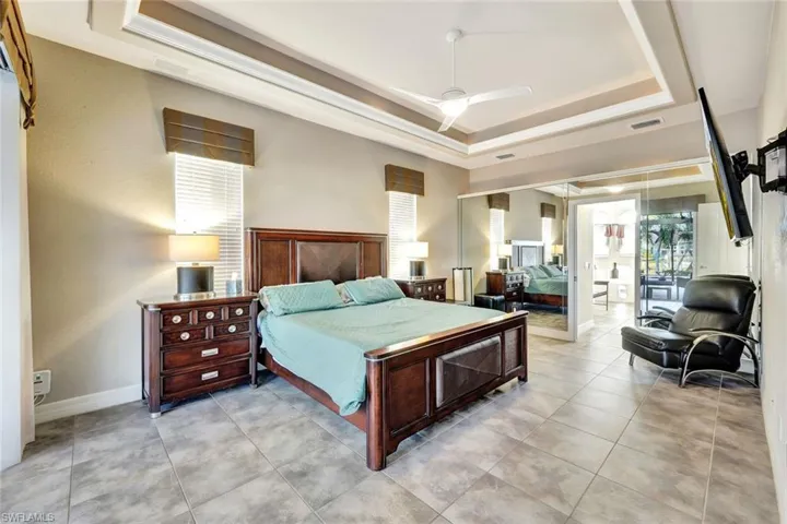Bedroom featuring a raised ceiling, multiple windows, and ceiling fan