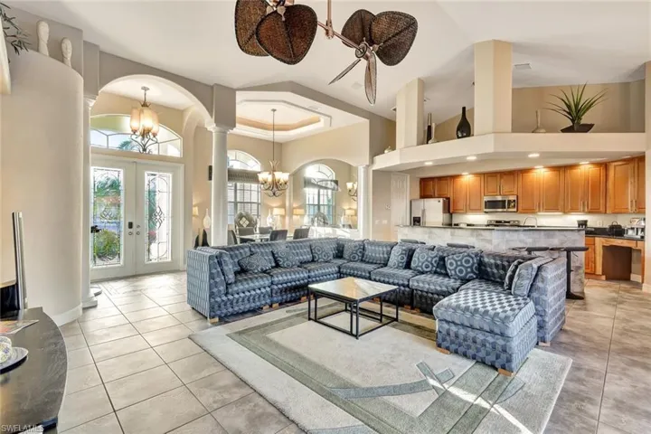 Living room featuring french doors, a towering ceiling, light tile patterned flooring, and ceiling fan with notable chandelier