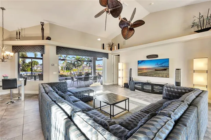 Living room with tile patterned flooring, high vaulted ceiling, and ceiling fan with notable chandelier