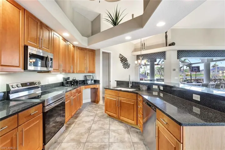 Kitchen featuring appliances with stainless steel finishes, a towering ceiling, sink, dark stone countertops, and hanging light fixtures