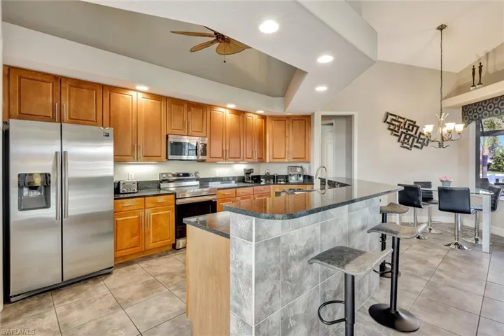Kitchen featuring a breakfast bar, ceiling fan with notable chandelier, sink, decorative light fixtures, and stainless steel appliances