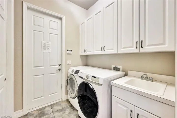 Washroom with cabinets, light tile patterned floors, washer and dryer, and sink