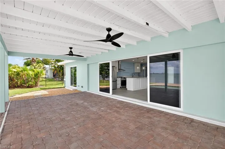 Spacious covered patio with brick paver flooring, exposed white wood beam ceiling, and two ceiling fans