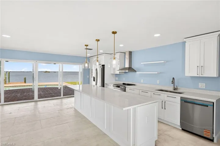 Open-concept kitchen featuring an expansive island with a light-colored countertop, white cabinetry, and stainless steel appliances