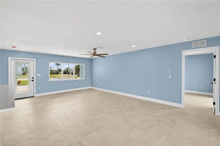 Spacious interior with neutral tile flooring, recessed lighting, a modern ceiling fan, and a large window overlooking exterior landscaping