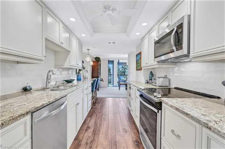Kitchen with stainless steel appliances, recessed lighting, dark wood finished floors, ornamental molding, and light stone counters
