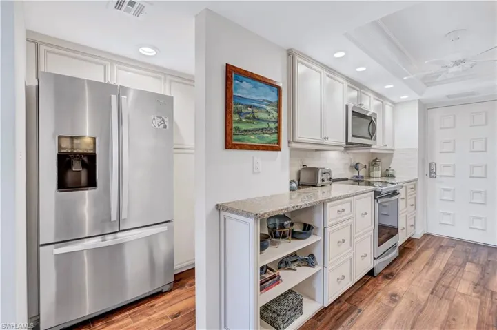 Kitchen featuring appliances with stainless steel finishes, decorative backsplash, wood finished floors, recessed lighting, and light stone counters