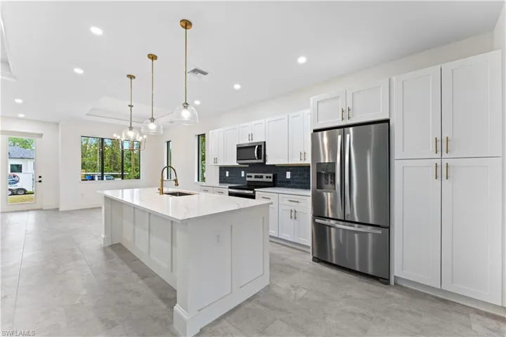 Kitchen with stainless steel appliances, hanging light fixtures, sink, an island with sink, and white cabinets