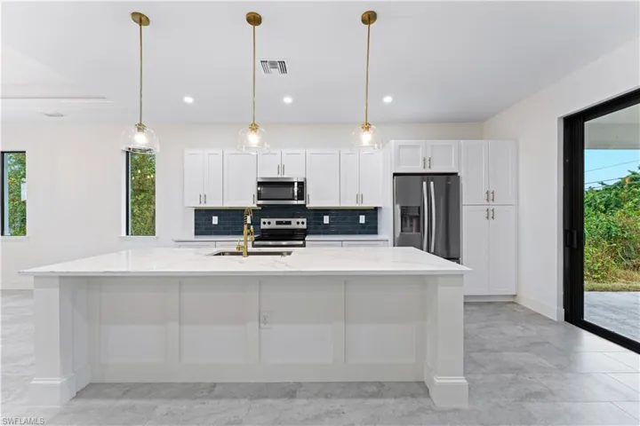 Kitchen with white cabinets, stainless steel appliances, a kitchen island with sink, and light white and grey quartz countertops