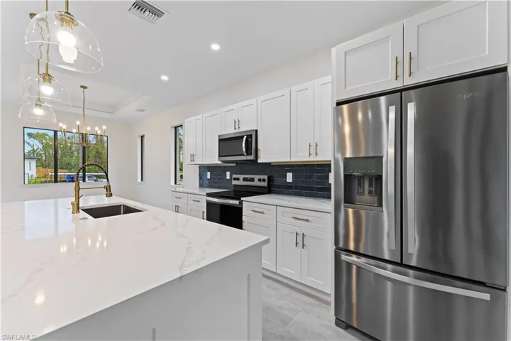 Kitchen with white cabinetry, stainless steel appliances, hanging light fixtures, and light stone countertops