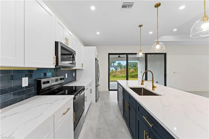 Kitchen with stainless steel appliances, white cabinetry, sink, tasteful backsplash, and hanging light fixtures