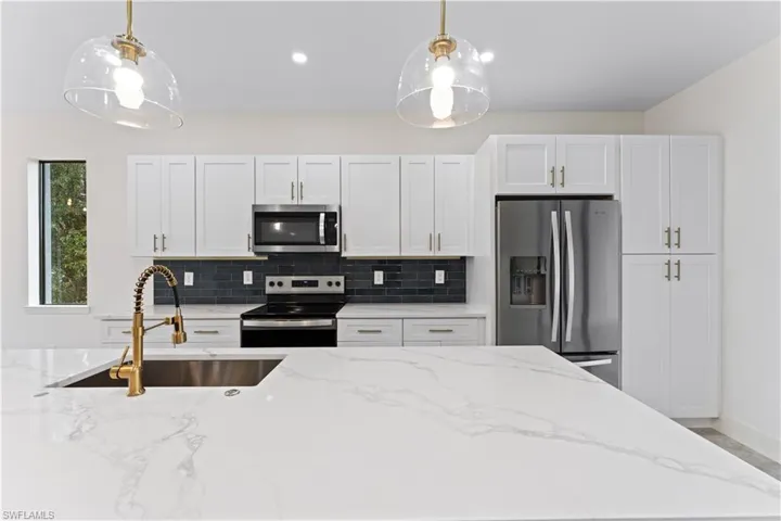 Kitchen with white cabinetry, stainless steel appliances, hanging light fixtures, and light stone counters