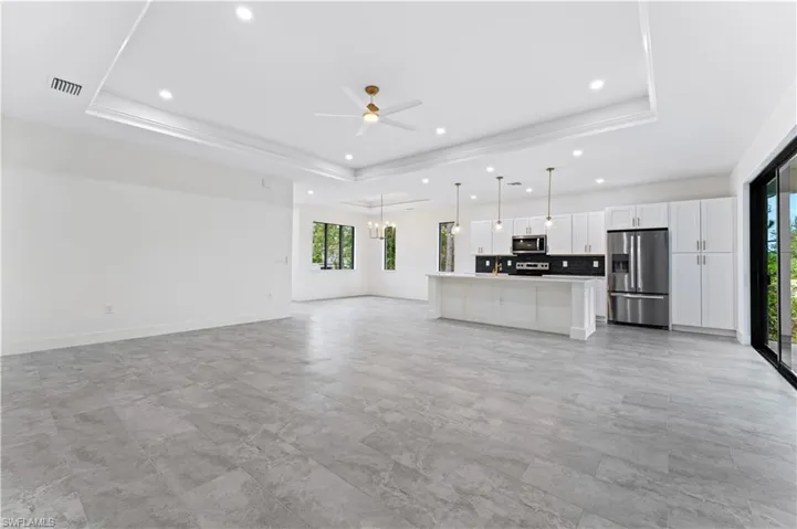 Unfurnished living room with ceiling fan with notable chandelier and a raised ceiling