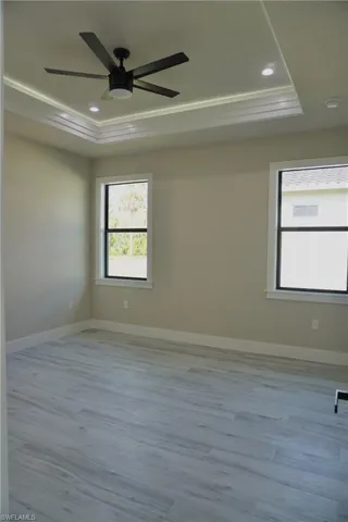 Unfurnished room featuring a tray ceiling, wood finished floors, baseboards, and ceiling fan