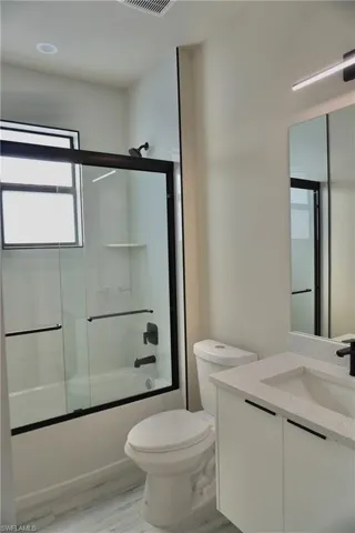 Bathroom with wood finished floors, vanity, bath / shower combo with glass door, toilet, and visible vents