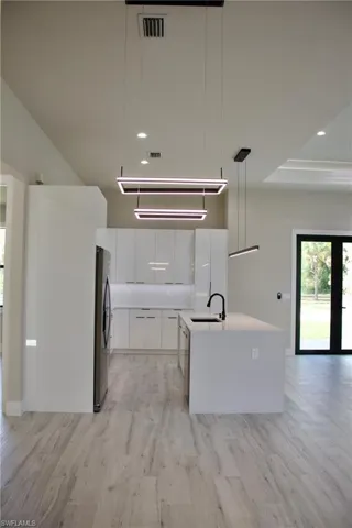 Kitchen with a sink, modern cabinets, freestanding refrigerator, light wood-style floors, and white cabinetry