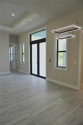 Unfurnished living room with french doors, a tray ceiling, light wood finished floors, baseboards, and ornamental molding