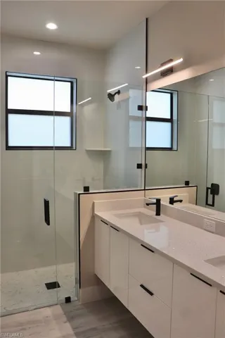 Full bath featuring wood finished floors, a sink, double vanity, and a stall shower