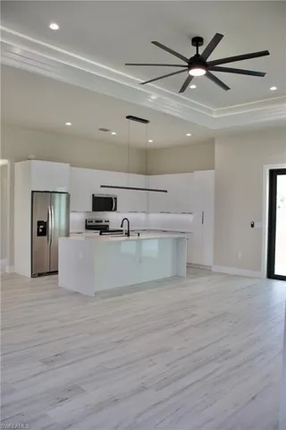 Kitchen with an island with sink, light wood-style floors, modern cabinets, stainless steel appliances, and white cabinetry