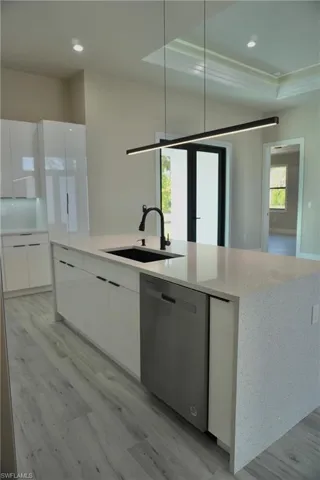Kitchen featuring stainless steel dishwasher, a sink, light wood-style floors, white cabinetry, and modern cabinets