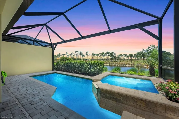 Pool at dusk with a lanai, an in ground hot tub, and a water view