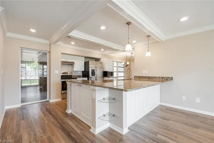 Kitchen with white cabinetry, vinyl plank flooring, crown molding, and appliances with stainless steel finishes