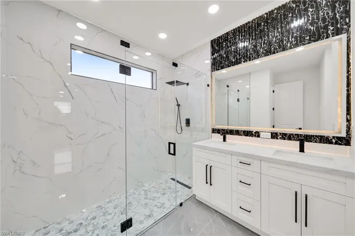 Bathroom featuring double vanity, a marble finish shower, recessed lighting, and stone wall