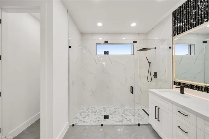 Full bathroom featuring vanity, a marble finish shower, healthy amount of natural light, recessed lighting, and light marble finish floors