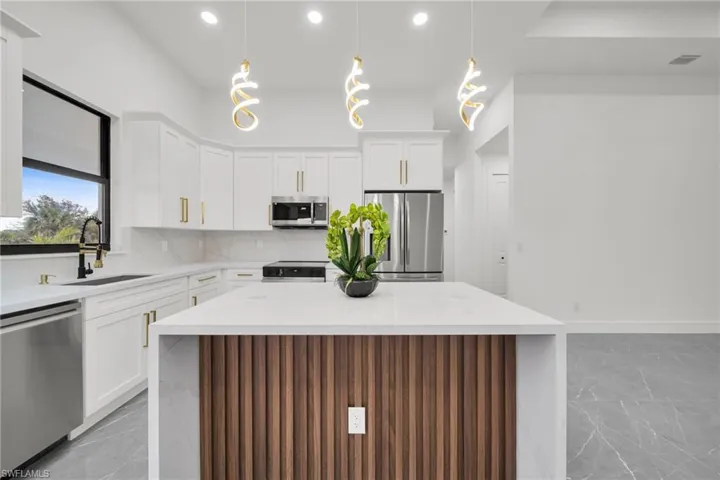 Kitchen with a kitchen island, tasteful backsplash, light stone counters, appliances with stainless steel finishes, and white cabinets