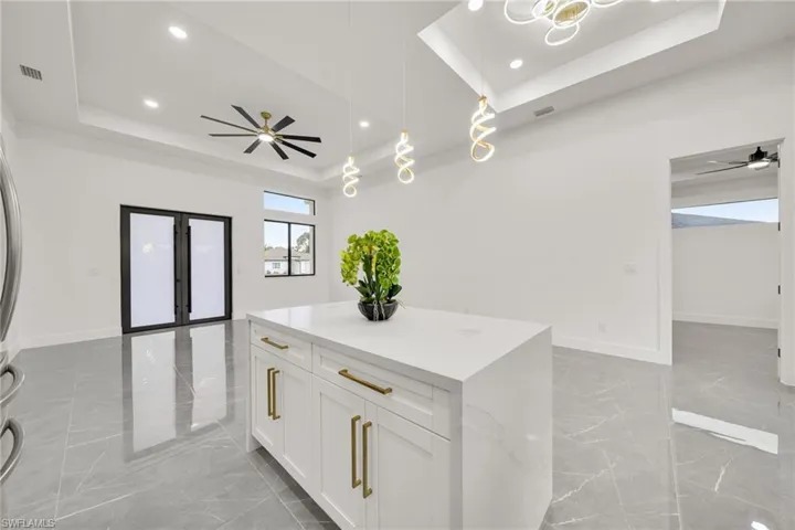Kitchen with ceiling fan, a tray ceiling, decorative light fixtures, white cabinets, and light marble finish flooring