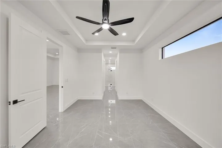 Unfurnished room featuring a raised ceiling, light marble finish floors, a ceiling fan, and recessed lighting