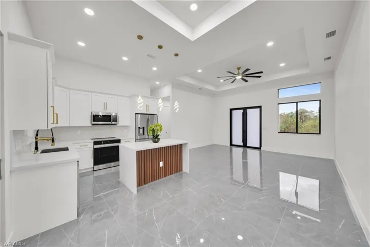 Kitchen featuring pendant lighting, open floor plan, light stone countertops, appliances with stainless steel finishes, and white cabinets
