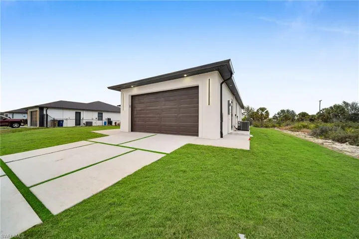 View of front of house featuring concrete driveway, a garage, stucco siding, a front lawn, and an outbuilding