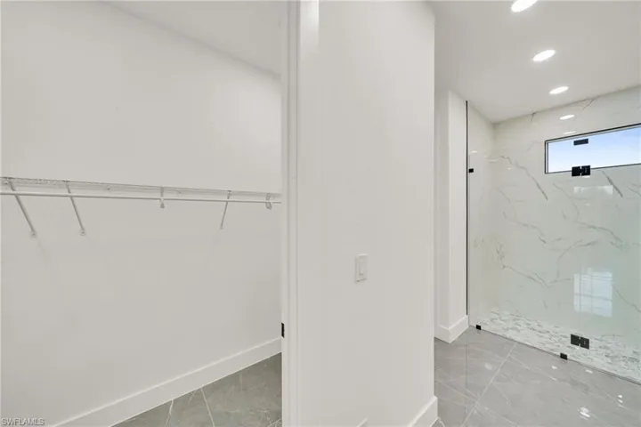 Bathroom featuring a spacious closet, a marble finish shower, light marble finish floors, and recessed lighting