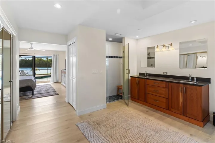 Full bathroom featuring double vanity, light wood finished floors, a stall shower, ensuite bath, and a water view