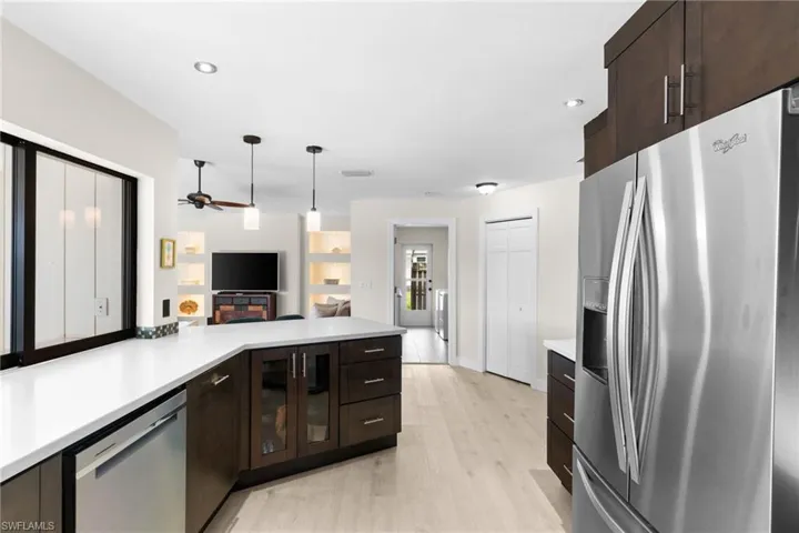 Kitchen featuring dark brown cabinetry, appliances with stainless steel finishes, hanging light fixtures, light wood finished floors, and recessed lighting