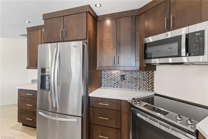 Kitchen featuring appliances with stainless steel finishes, decorative backsplash, dark brown cabinetry, light stone counters, and recessed lighting