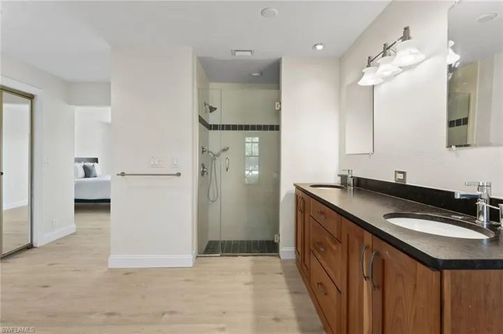 Ensuite bathroom featuring double vanity, light wood-style floors, and a shower stall