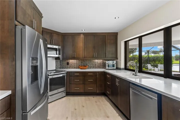 Kitchen featuring stainless steel appliances, dark brown cabinetry, backsplash, light wood-type flooring, and recessed lighting
