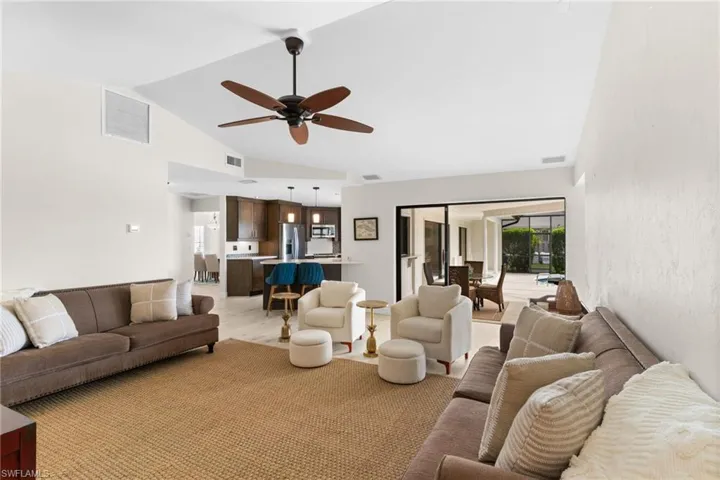 Living area with vaulted ceiling, a ceiling fan, and light wood-style flooring