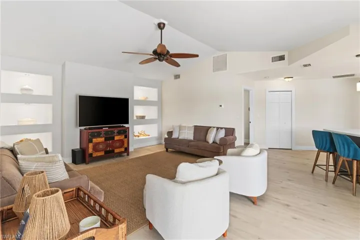 Living room featuring built in shelves, light wood-type flooring, lofted ceiling, and a ceiling fan