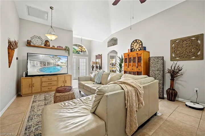 Living room with french doors, a ceiling fan, arched walkways, light tile patterned flooring, and high vaulted ceiling