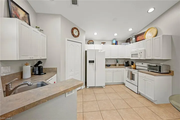 Kitchen with white appliances, white cabinetry, light countertops, recessed lighting, and light tile patterned floors