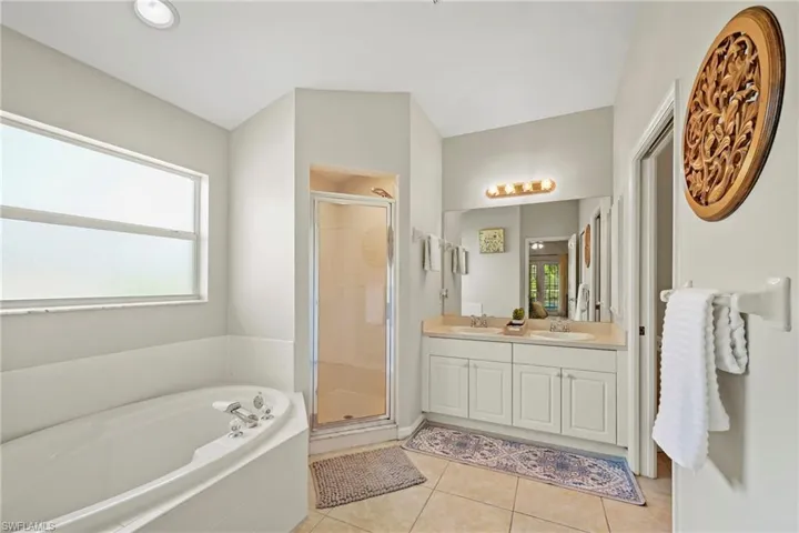 Full bathroom with double vanity, a shower stall, a bath, and light tile patterned floors