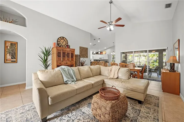 Living area featuring high vaulted ceiling, light tile patterned flooring, a ceiling fan, and arched walkways