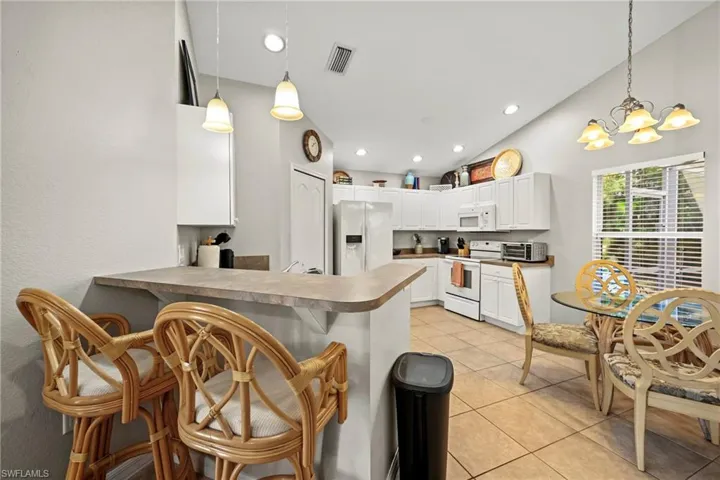 Kitchen featuring a kitchen bar, white appliances, hanging light fixtures, a peninsula, and white cabinetry