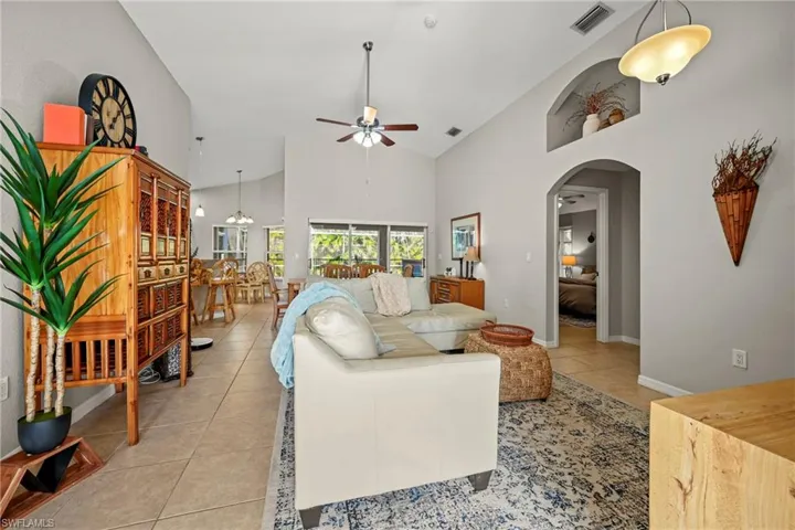 Living room featuring light tile patterned flooring, high vaulted ceiling, ceiling fan, and arched walkways